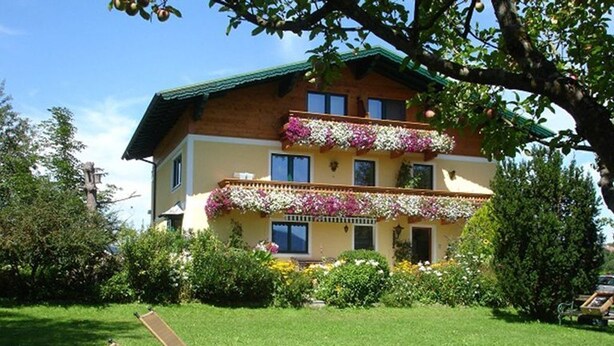A two-story building with balconies, a lawn, and a tree. - Spatzennest apartment in country house style - Anna Laireiter (Keuschen)