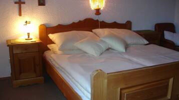 Ein hölzernes Bett mit weißer Bettwäsche, ein Nachttisch mit Lampe und ein an der Wand befestigtes Kreuz.