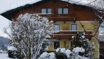 Ein zweistöckiges Gebäude mit Balkon, umgeben von schneebedeckten Bäumen.