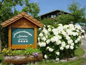 Ein hölzernes Schild, ein weißer Hortensienstrauch und ein Haus im Hintergrund.