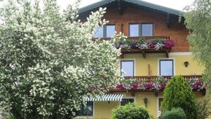 A two-story building with balconies, a wooden facade, and flower boxes. - Spatzennest apartment in country house style - Anna Laireiter (Keuschen)