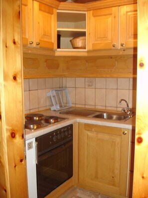 A compact kitchen with wooden cabinets, a stove, an oven, a sink, and a toaster.