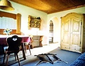 Ein Zimmer mit Esstisch, Stühlen, einer Couch, einem Schrank und einer Decke mit Holzbalken.