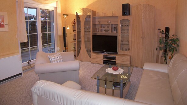 Een woonkamer met een glazen salontafel, een bank, een tv-meubel met planken, en een schuifdeur naar buiten.