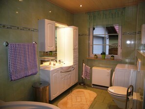 Une salle de bain avec un lavabo, un miroir et des toilettes. Une serviette est accrochée au mur et il y a une poubelle.
