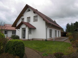 Une maison à deux étages avec un toit en pente, une entrée principale et une allée pavée.