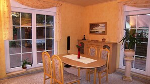Een eethoek met een ronde tafel, zes stoelen, een vaas met een rode bloem, een schilderij aan de muur en een potplant.