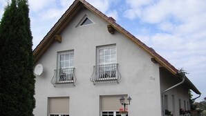 Een gebouw met twee verdiepingen, een grijze gevel, twee balkons met metalen hekwerk en een schotelantenne aan de linkerzijde.
