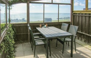 Eine überdachte Terrasse mit Tisch und Stühlen, mit Blick auf die Küste.