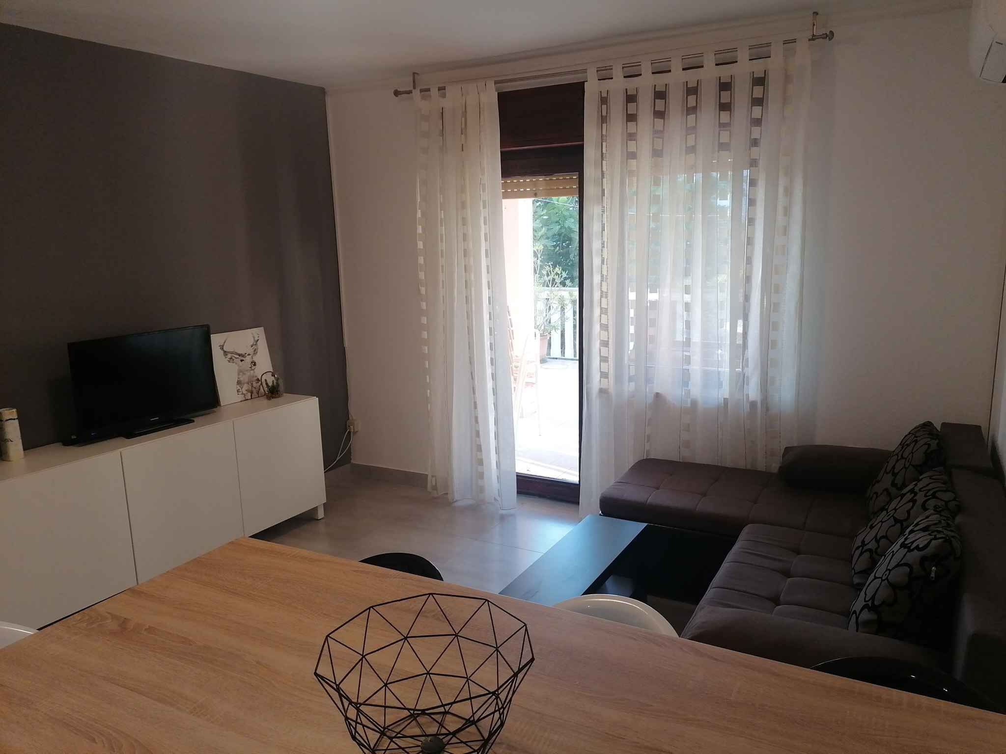 A modern living room with a sofa, a TV on a cabinet, and a wooden table.