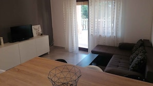 A modern living room with a sofa, a TV on a cabinet, and a wooden table. - Holiday apartment mit Terrasse (Šilo)