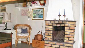 A cozy living room with a brick fireplace, a wicker chair, a small table with a lamp, and a bookshelf. - Amazing home in Hagfors (Hagfors)