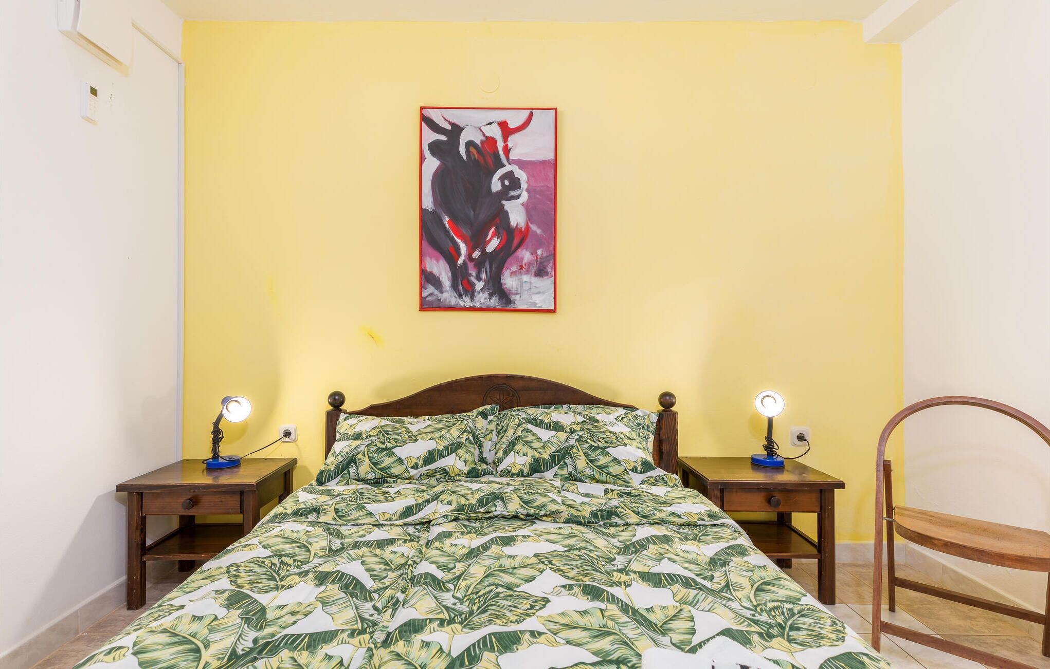 A bedroom with a bed, two bedside tables, a chair, and a wall-mounted painting.