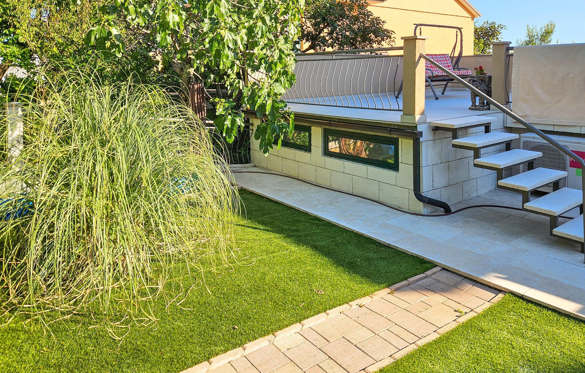 Un espace patio avec un petit coin salon extérieur, un escalier et une pelouse bien entretenue.