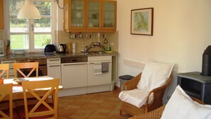 A compact kitchen with wooden cabinets, a dining table with chairs, and a wicker sofa. - Landschek, Holiday home Das Ulmenhaus - Holiday home (Rankwitz)