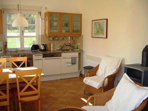 Een compacte keuken met houten kastjes, een eethoek met rieten stoelen en een inbouwfornuis.