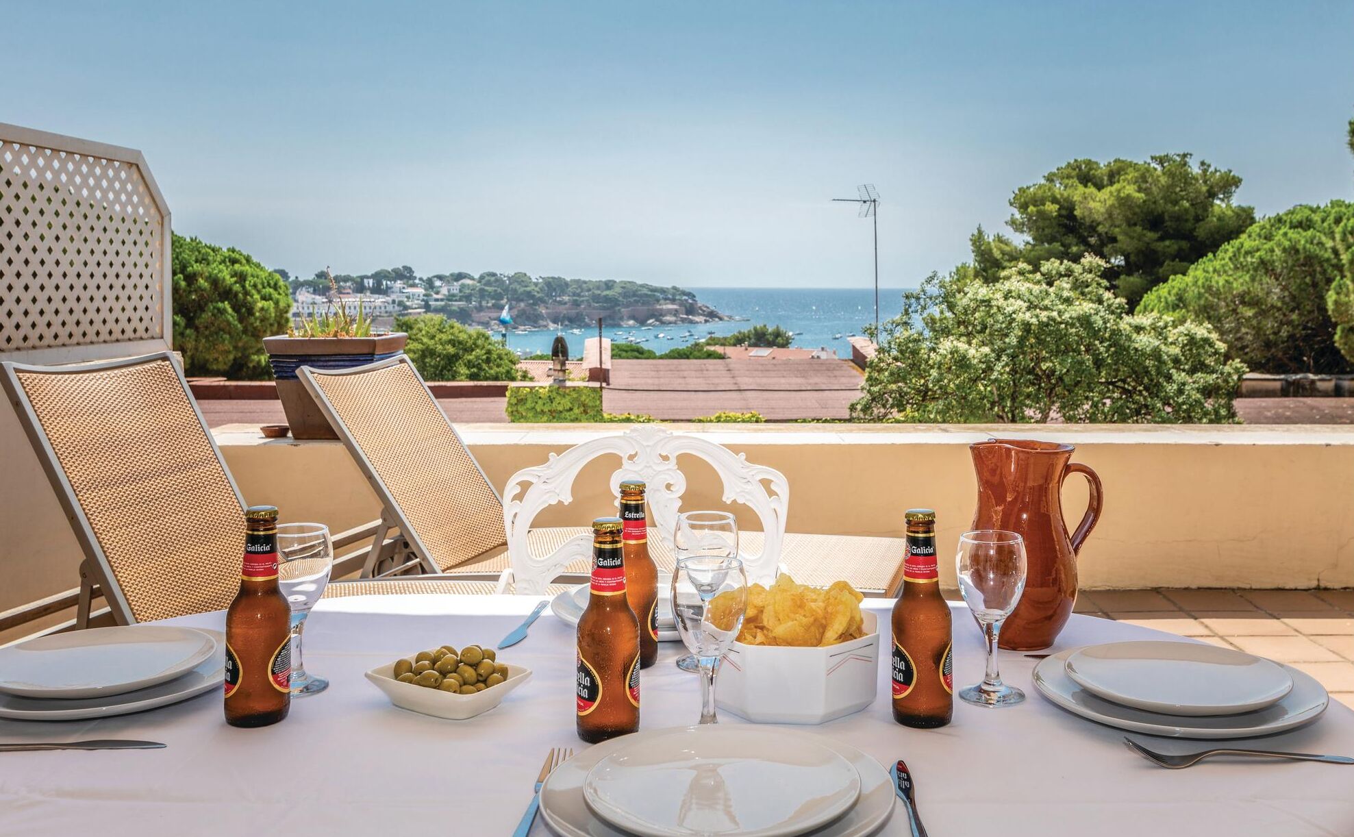 A table set for two with bottles of beer, a bowl of olives, and a pitcher, overlooking a scenic coastal view.