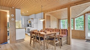 A cozy cabin interior with a wooden dining table, chairs, a sofa, and a kitchen area. - 3 bedroom lovely home in Sæby (Sæby)