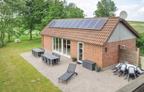 Een bakstenen huis met schuin dak, zonnepanelen en een terras met tafels en stoelen.