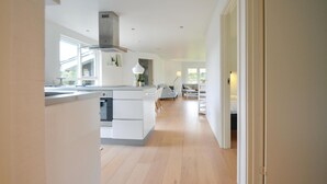 Et moderne køkken med en central ø, et spiseområde med en sofa og udsigt til det fri.
