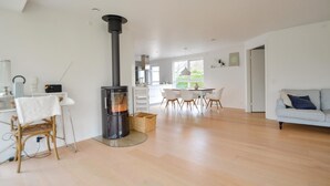 En moderne stue med brændeovn, spiseplads med hvidt bord og stole, samt en lysegrå sofa.