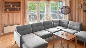Een moderne woonkamer met een grijze modulaire bank, een houten salontafel en een groot raam met uitzicht op groen.