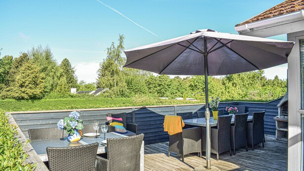 Een terras buiten met rieten meubels, een tafel en een parasol.