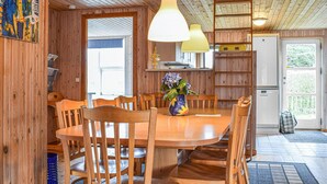 Een houten eethoek met een ronde tafel en stoelen, een vaas met bloemen en hanglampen.