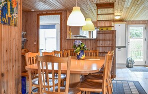 A wooden dining area with a round table and chairs, a vase with flowers, and pendant lights.