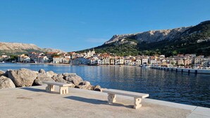 Une promenade en bord de mer, agrémentée de bancs, offrant une vue dégagée sur une ville côtière et s’étendant sur un terrain rocheux en arrière-plan.