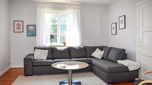 Un salon moderne avec un canapé d’angle gris, une table basse ronde et un tapis blanc.