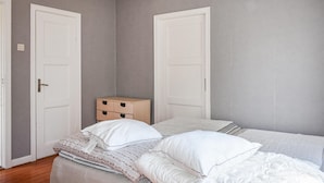 Une chambre avec deux lits, une petite commode en bois et deux portes blanches.
