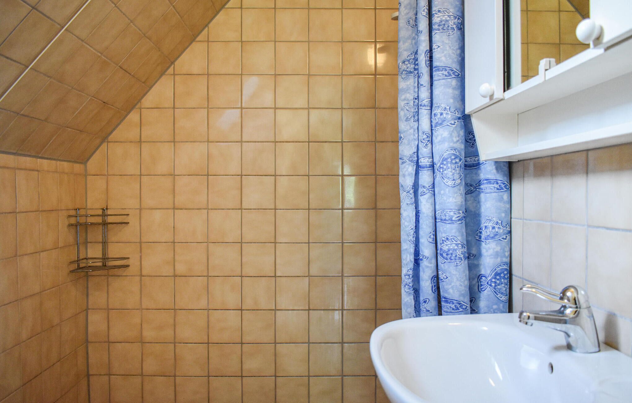 Ein Badezimmer mit weißem Waschbecken, einer Dusche mit blumigem, blauen Vorhang und einer gefliesten Wand.