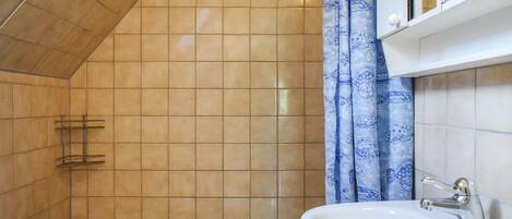 Ein Badezimmer mit weißem Waschbecken, einer Dusche mit blumigem, blauen Vorhang und einer gefliesten Wand.