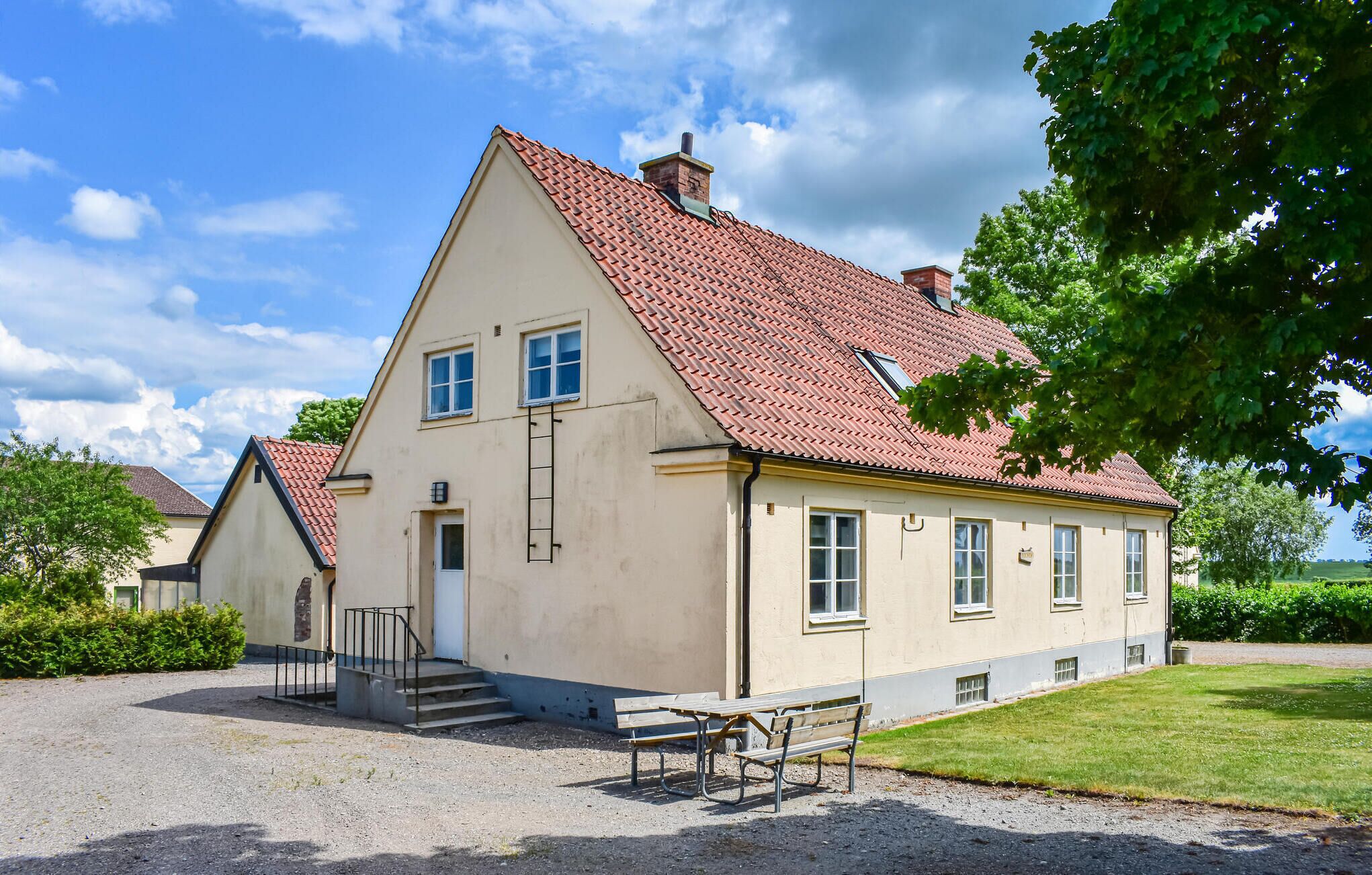 A two-story building with a red-tiled roof, a visible chimney, and a small front porch with steps leading to the entrance.