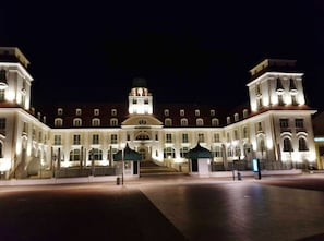 Un grand bâtiment illuminé, doté d’un dôme central et de deux ailes symétriques, avec une entrée monumentale et une tour horloge.