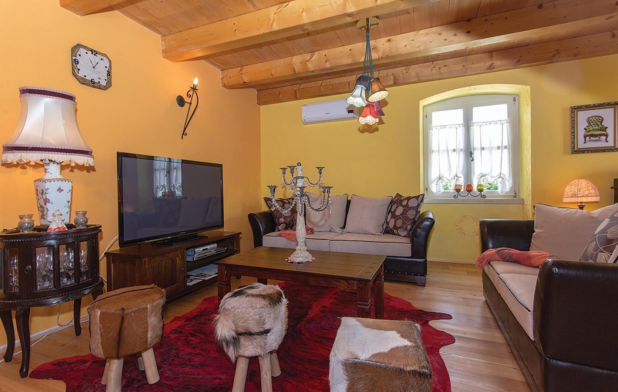 Ein gemütliches Wohnzimmer mit Holzbalkendecke, einem Fernseher, einem Sofa, einem Couchtisch und einem roten Teppich.