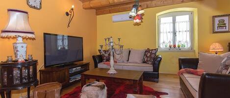 Ein gemütliches Wohnzimmer mit Holzbalkendecke, einem Fernseher, einem Sofa, einem Couchtisch und einem roten Teppich.