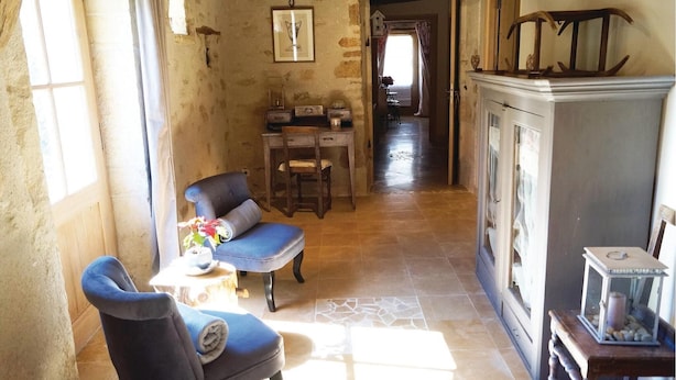 A rustic room with a stone wall, a wooden cabinet, a blue armchair, a small table with a lamp, and a window with curtains. - Stunning home in RUFFEY LES BEAUNE (RUFFEY LES BEAUNE)