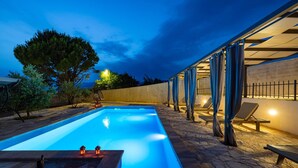 Ein rechteckiger Pool mit einer Steindeck, umgeben von Liegestühlen und einer Pergola mit blauen Vorhängen.
