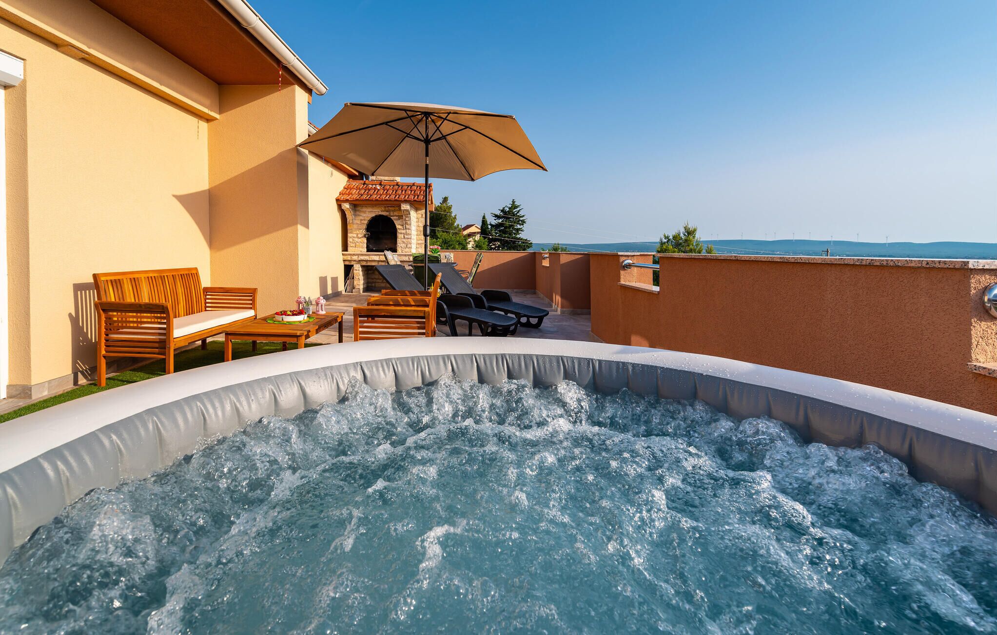 A hot tub with a stone fireplace, outdoor seating, and a clear view of the sea.