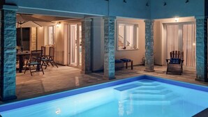 Et poolområde med en klar pool, stenkolonner og et spiseområde med stole og et bord.