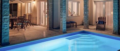 A pool area with a clear pool, stone pillars, and a dining area with chairs and a table.