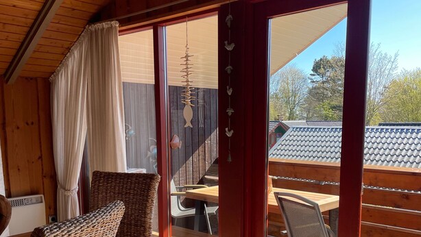 A wooden interior with wicker furniture, a sliding glass door leading to an outdoor patio with a table and chairs.
