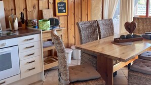 A wooden interior with a dining table, wicker chairs, a kitchen area, and a sign indicating fish & chips for 5€.
