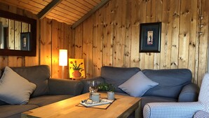 A wooden interior with a sofa, a table with a lamp, and a framed picture on the wall.