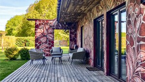 Een overdekt terras met rieten meubels, een houten terras en een muurschildering met bloemenmotieven.