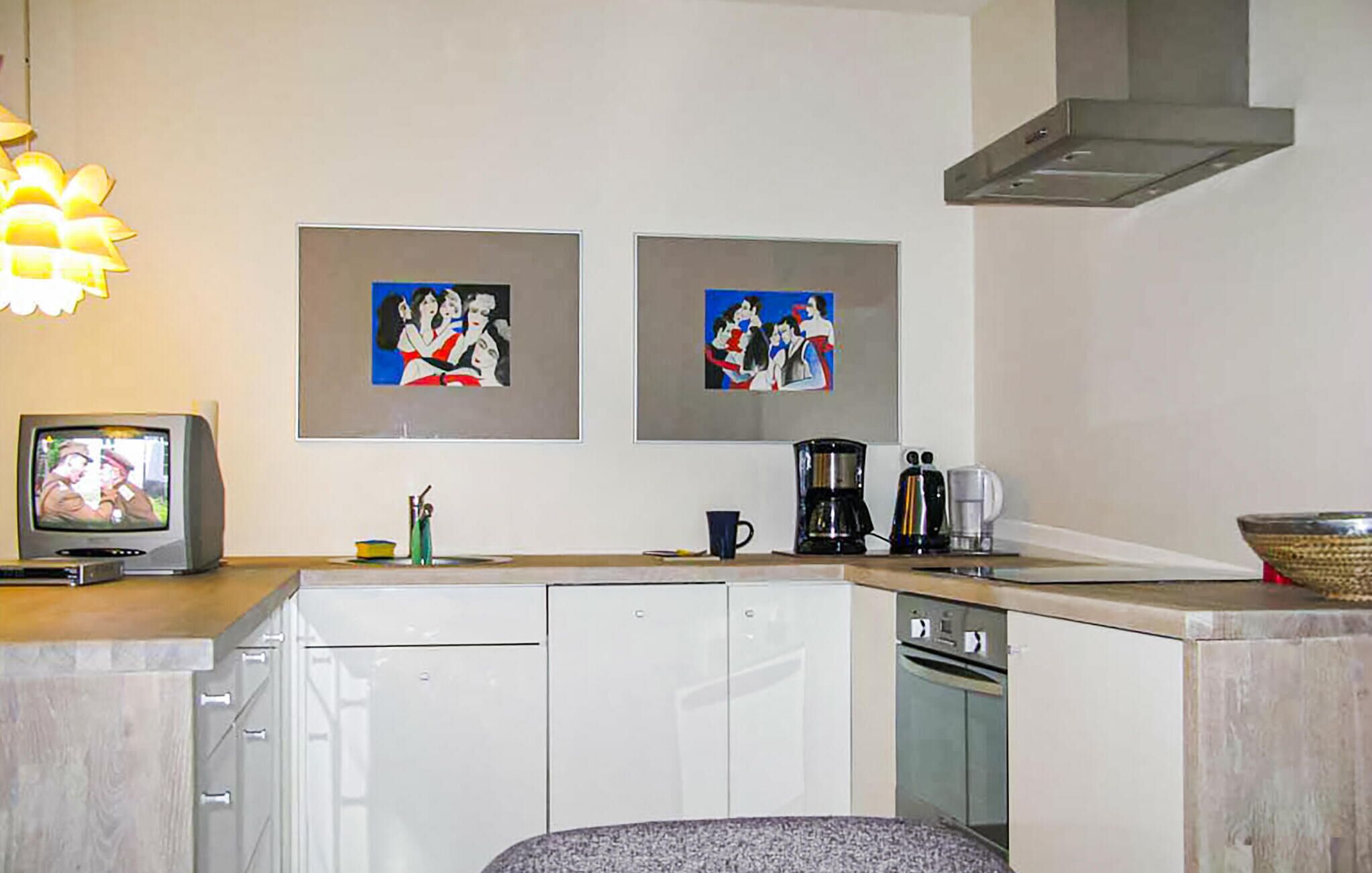 A kitchen with white cabinets, a coffee maker, and two framed paintings on the wall.