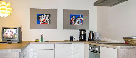 A kitchen with white cabinets, a coffee maker, and two framed paintings on the wall.