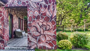 Een gebouw met een grote bloemenmuur aan de buitenkant, een overdekt terras en een tuin met diverse planten en bomen.